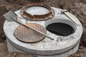 Installation of a reinforced concrete well for water supply and sewerage at the construction site. Well rings with cast iron hatch and construction tool.
