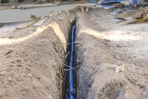 Laying a blue electrical cable in a trench in the ground. Underground communications. Electrical work at the construction site.